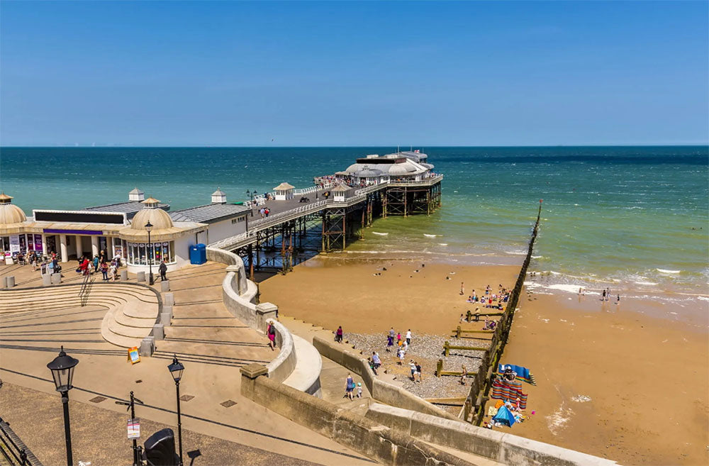 Sheringham pier extending into the ocean with people on a sandy beach below, under a clear blue sky.