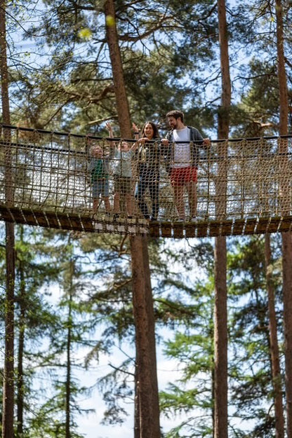 Family on a treetop adventure bridge in a forest at BeWILDerwood. BeWILDerwood is an award-winning, whimsical outdoor woodland adventure park for families, with locations in England. Based on books by author Tom Blofeld, it offers imaginative, nature-based play, including treetop mazes, wobbly wires, slippery slides, boat rides, and character-driven storytelling for children aged 2 to 12.