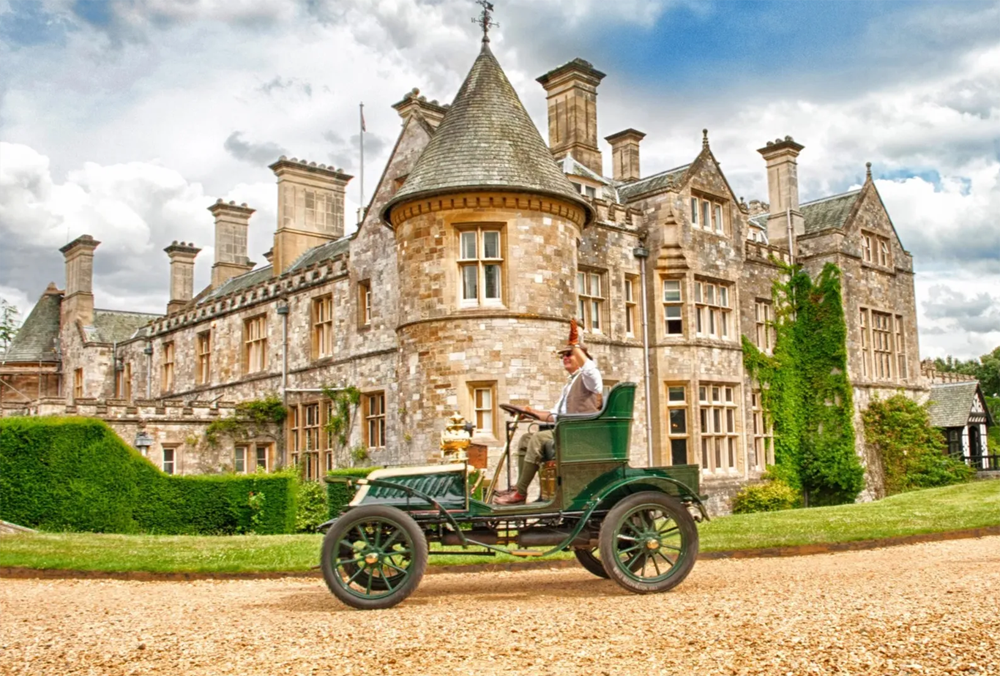 Vintage car in front of a Beulieu House with a person sitting inside. The National Motor Museum at Beaulieu, located in England's New Forest, houses a world-famous collection of over 280 vehicles and motoring memorabilia, documenting British motoring history. Founded in 1952, the museum showcases iconic cars, land speed record breakers, Formula 1 machines, and classic motorcycles, alongside exhibits like "On Screen Cars" and "World of Top Gear"