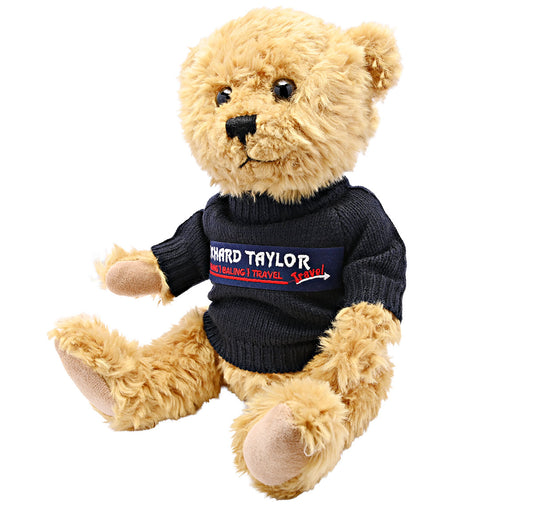 Bill The Bear plush teddy bear with light tan fur wearing a black knit turtleneck sweater with a 'Richard Taylor Travel' logo on the chest, set against a plain white background.