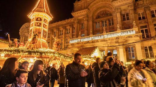 People gathered around Birmingham Christmas market with a decorated building in the background and festive atmopshere.