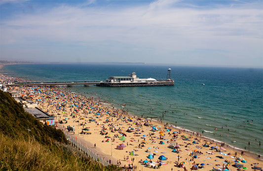 Bornemouth coastal beach scene with people, umbrellas, and a pier on a sunny day.