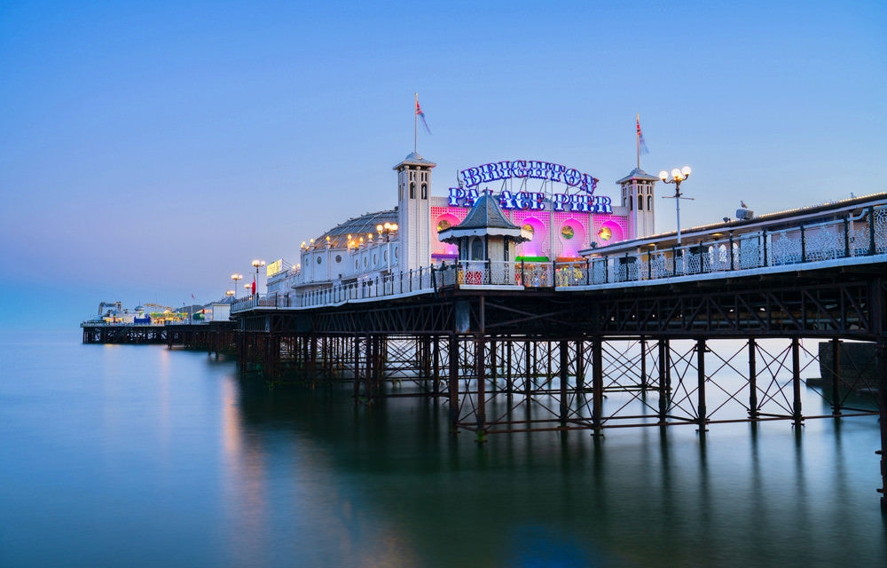 Brighton Pier with a colourful sign at dusk, surrounded by water.
