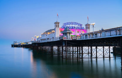 Brighton Pier with a colourful sign at dusk, surrounded by water.