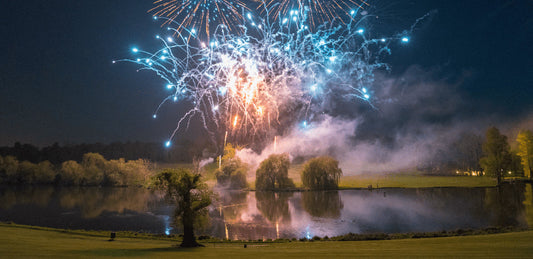 Firework display over Brocket Hall lake with trees and grounds in the scene