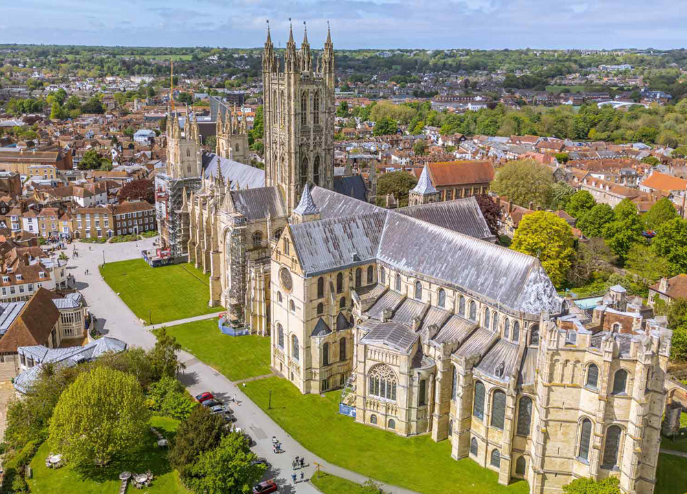 Aerial view of Canterbury Cathedral with greenery and roads and surrounding area. Canterbury Cathedral, located in Kent, is one of England’s most significant Christian structures, serving as the Mother Church of the worldwide Anglican Communion and the seat of the Archbishop of Canterbury. Founded in 597 AD by St. Augustine, this UNESCO World Heritage Site is famous as the site of Thomas Becket's 1170 murder and is often called "England in stone".
