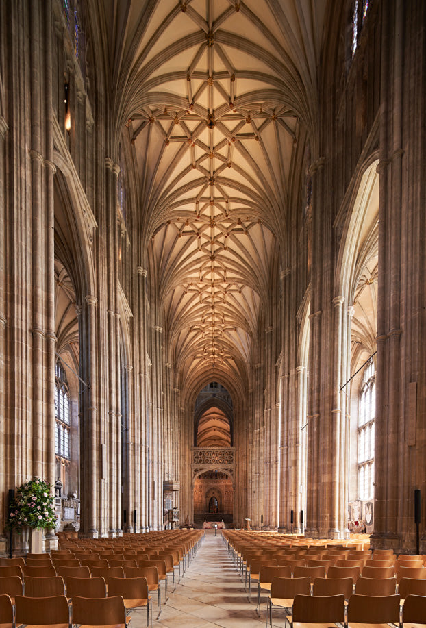 Narrow shot of a Canterbury Cathedral interior with high vaulted ceilings and rows of pews. Canterbury Cathedral's interior is a vast, awe-inspiring mix of Romanesque and Gothic architecture, featuring a high-vaulted perpendicular nave, the historic 12th-century quire, and the tranquil Trinity Chapel. Key features include stunning medieval stained glass, the Martyrdom spot of Thomas Becket, the ancient crypt, and the stone screen with royal statues.