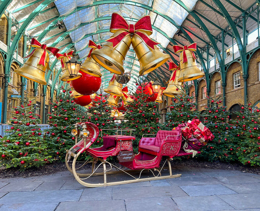 Decorative Christmas scene with gold bells, red bows, and a pink sleigh in Covent Garden indoor market setting in London UK.