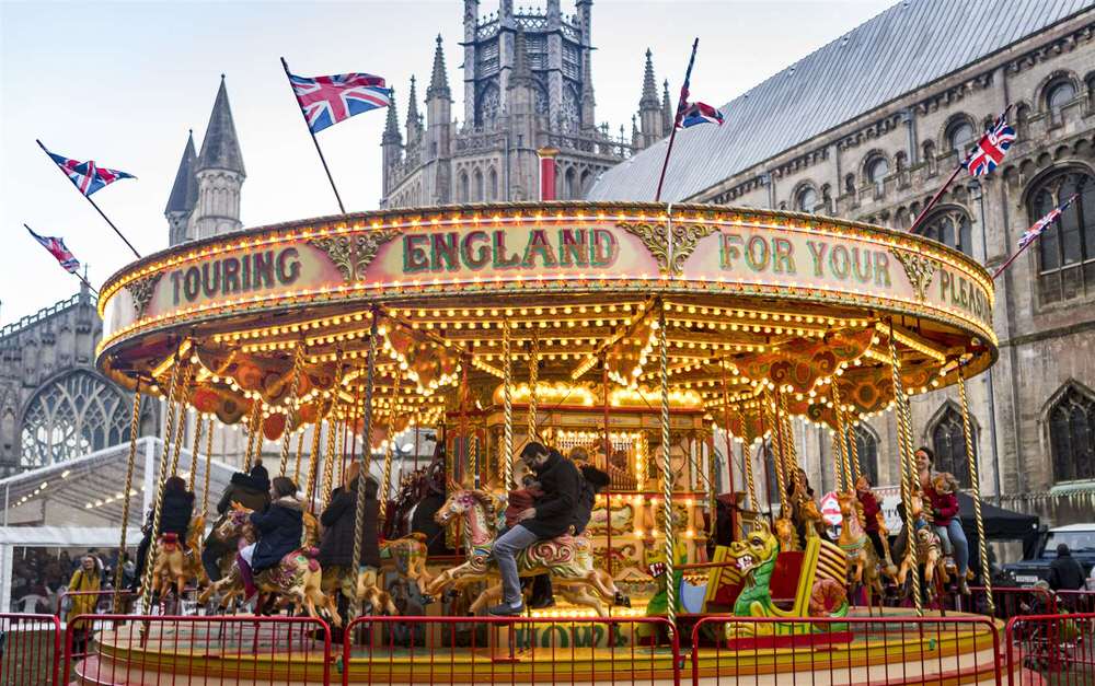 Carrousel with 'Touring England For Your Pleasure' sign in front of Ely cathedral at their famous Christmas Fair. 