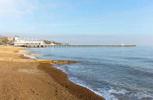 Felixstowe beach with a pier extending into the ocean under a clear blue sky.