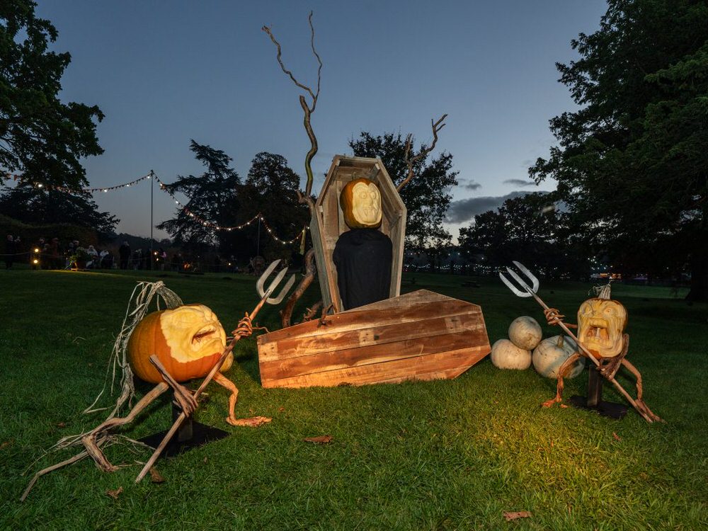Halloween-themed decoration with professionally carved pumpkins, coffin, and skeleton in a Trentham gardens