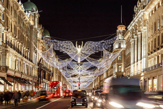 Decorative London Christmas lights in the shape of an angel hanging above a city street at night. Featuring blurred traffic and festive atmosphere.
