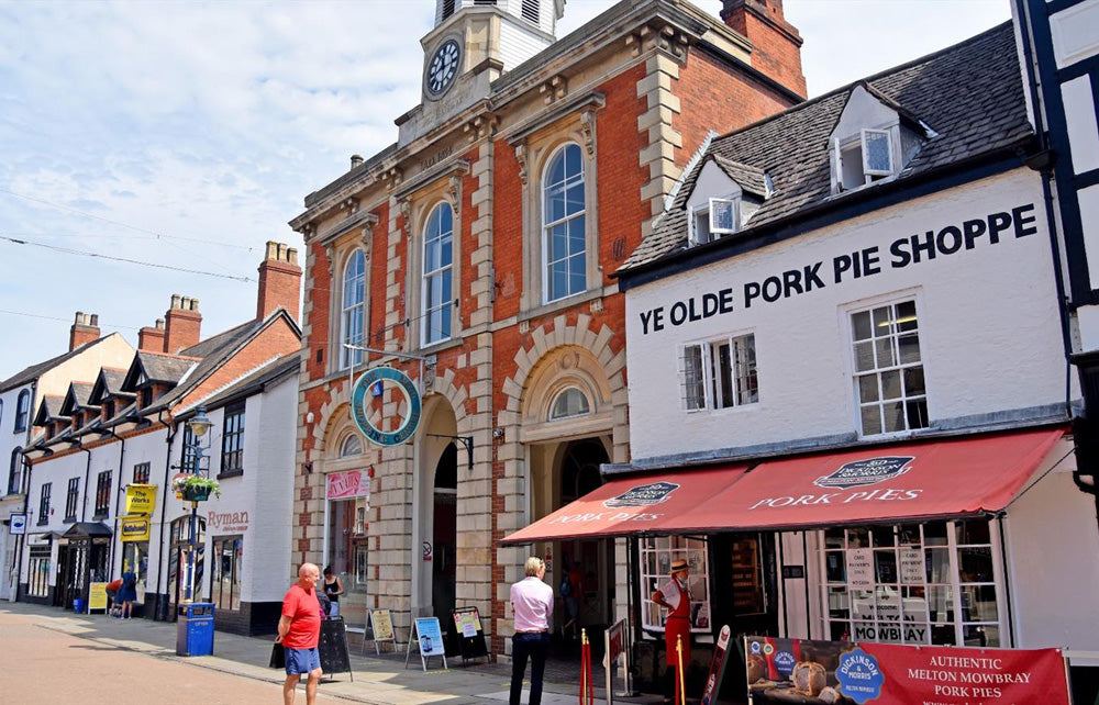 Melton Mowbray High Street and 'Ye Olde Pork Pie Shoppe' building. Melton Mowbray high street is a bustling, historic, and quintessentially English market town centre, characterized by charming older buildings, a lively atmosphere, and a strong "foodie" focus. It serves as a, central hub for local shopping, featuring traditional pork pie shops, artisan food retailers, cafes, and easy access to the adjacent vibrant market.
