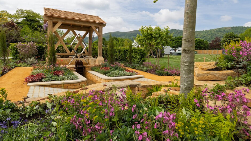 Garden with wooden gazebo, pathways, and colourful flowers under a blue sky at RHS Malvern. The RHS Malvern Spring Festival is a premier annual horticultural event held at the Three Counties Showground, Worcestershire, marking the start of the summer gardening season. It features renowned show gardens, a vast Plant Village, floral marquees, and celebrity experts like Monty Don. The festival offers food, shopping, and family activities in a scenic setting.