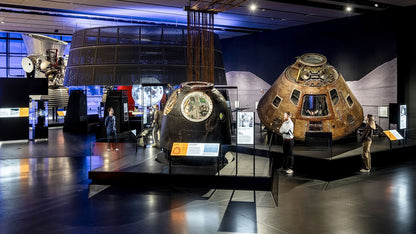Museum exhibit with space capsules and visitors in a darkened room at The Science Museum. Located in South Kensington, London, the Science Museum is a world-renowned institution offering free, interactive exploration of science, technology, engineering, and medicine. It features seven stories of educational exhibits, including iconic objects like the Apollo 10 capsule, early steam engines, and the Wonderlab, designed to inspire curiosity in visitors of all ages.