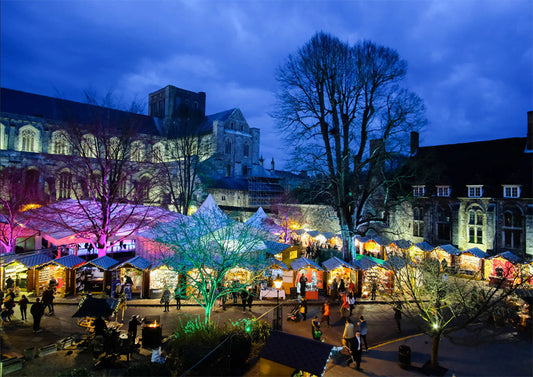 Night time outdoor Christmas market at Winchester with colourful lights and people walking around.
