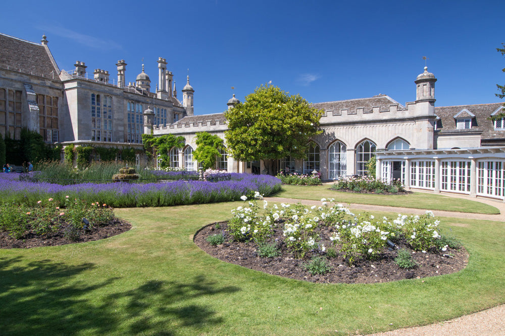 Historic Burghley House with a well-maintained garden featuring flowers and trees under a clear blue sky. Burghley House is a magnificent 16th-century Elizabethan "prodigy house" near Stamford, Lincolnshire, built by Sir William Cecil, Queen Elizabeth I’s Lord High Treasurer. It is known for its grand, symmetrical Elizabethan design, extensive Renaissance art collection, and stunning interiors with painted ceilings. Surrounded by a Capability Brown-landscaped park, it is a leading English stately home.
